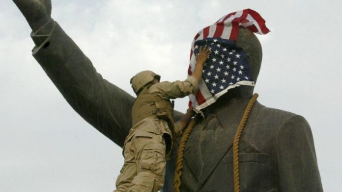 Un infante de marina estadounidense cubre el rostro de la estatua de Saddam Hussein en Bagdad días después de la invasión. La estatua luego fue derribada, convirtiéndose en una símbolo del derrocamiento del líder iraquí. GETTY
